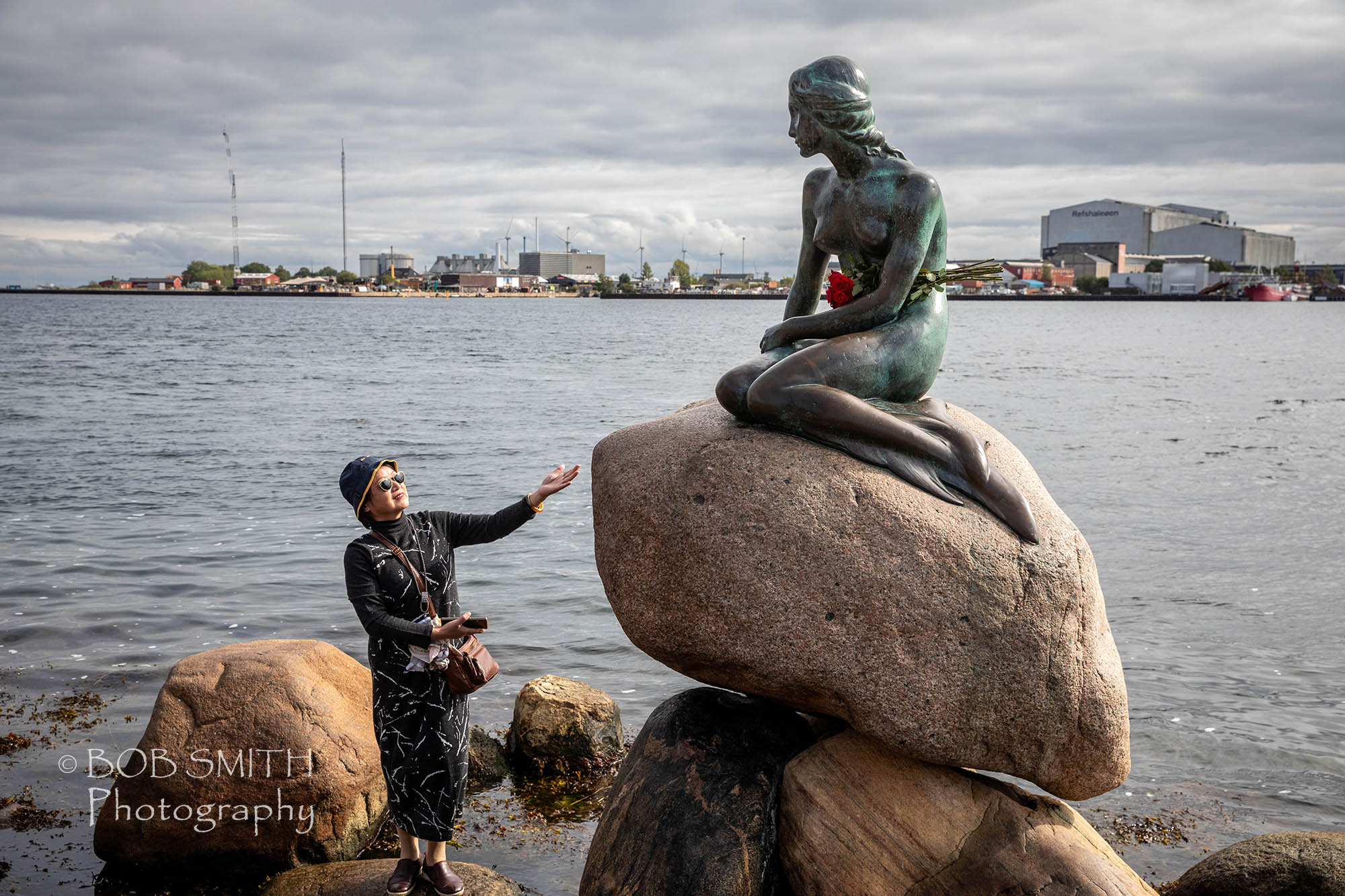 A visitor with the statue of the Little Mermaid in Copehagen harbour.